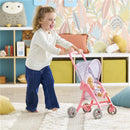 Young child joyfully pushes a pink floral pushchair accessory with a 30 cm doll inside, on a carpeted floor.