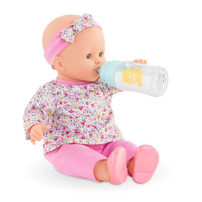 Magic Milk Baby Doll with floral outfit and pink headband, drinking from a baby bottle with a cartoon character.