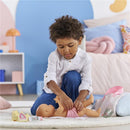 Child playing with a Corolle dolls accessory set, changing the outfit of a baby doll on a soft blanket, with accessories nearby.