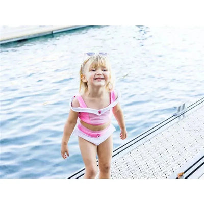 Girl in a pink two-piece swimsuit smiles while playing near the water, showcasing the Creative Education - 2Pk Swim Suit.