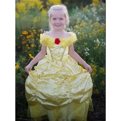 A young girl smiles while wearing a yellow Disney Belle dress with a red rose detail, standing in a field of flowers.