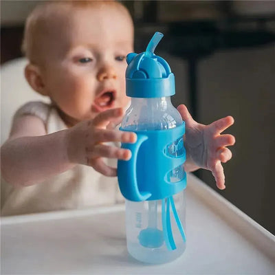 Narrow blue sippy straw bottle with silicone handles, held by a child reaching out, encouraging independent drinking.