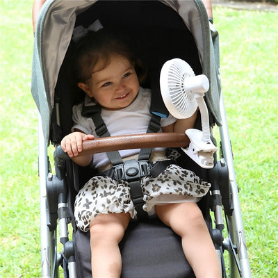 Cage stroller fan attached to a stroller, blowing air towards a smiling toddler wearing a white shirt and patterned shorts.