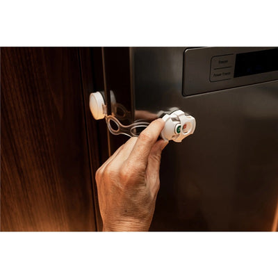 Hand installing a Dreambaby Ezy-Check Multi-Use Latch on a refrigerator, showing the latch mechanism and its safety design.