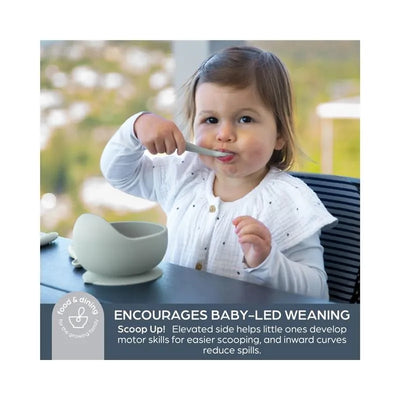 A child is using a spoon to eat from a seafoam-colored Scoop Suction Bowl, designed to promote baby-led weaning.