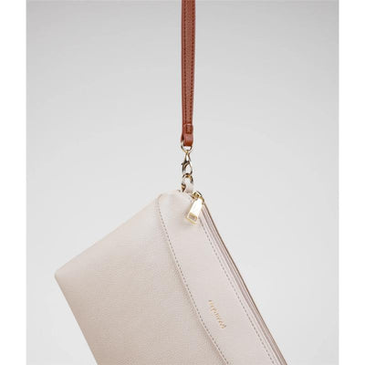 Light beige Nova Bag by Enya Mond, featuring a gold zipper and a brown strap, hanging against a neutral background.