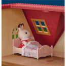 Calico Critters rabbit doll in a pink bed with a floral blanket inside a cozy cottage bedroom.