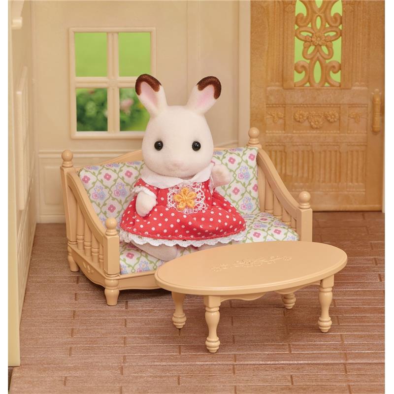 Calico Critters rabbit figurine in red polka dot dress sits on a beige couch with floral cushion in a dollhouse interior.