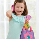 Toddler girl smiling while holding a toy phone and a credit card, with a colorful purple purse featuring a flower design.