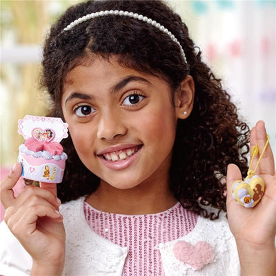 Girl holding a colorful cupcake toy and a heart-shaped pendant from the Epoch - Pati-School Disney Princess Creations Kit.
