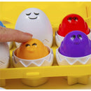 Brightly colored plastic eggs in a yellow holder, with a finger touching a smiling orange egg, part of a baby matching toy.