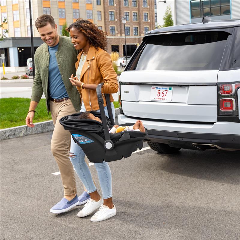 Couple walking together in a parking lot, carrying a baby in Evenflo Shyft Dualride Infant Car Seat, near a white vehicle.