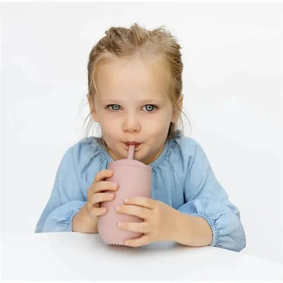 Young girl with blue eyes drinking from a sage-colored Ezpz Happy Cup with a straw.