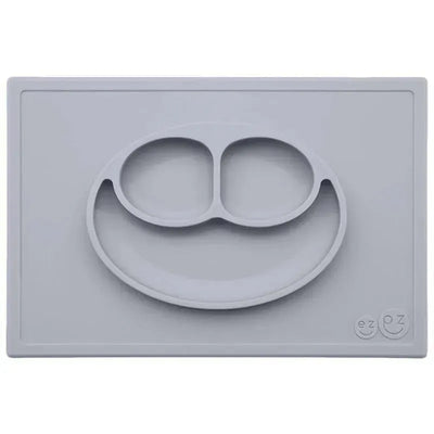 Silicone feeding mat in pewter color featuring a smiling face design with two compartments.