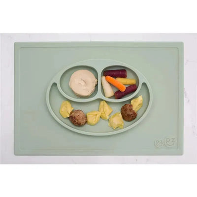 Sage green silicone plate with compartments holding meatballs, dumplings, vegetables, and mashed potatoes.