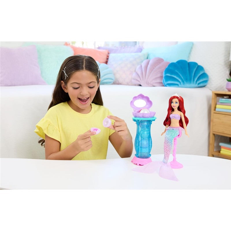 A girl in a yellow shirt excitedly examines a pink shell while playing with the Fisher Price Disney Princess Ariel Mermaid playset.