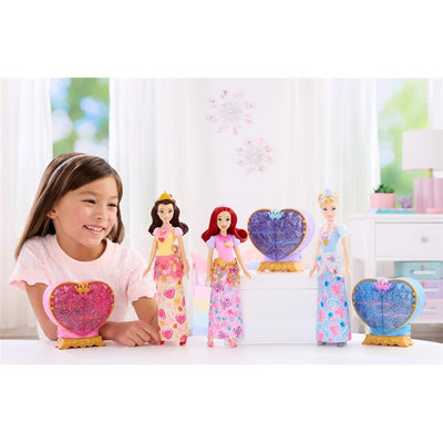 Young girl smiles while playing with Fisher Price Disney Princess dolls, featuring Belle, Ariel, and Cinderella, in a bright setting.
