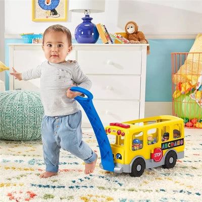 Toddler pulls a Fisher Price Little People school bus toy with colorful characters inside, promoting early learning and play.