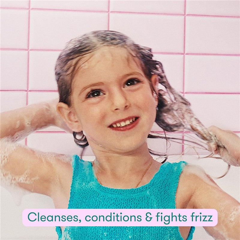 Child washing her hair with the Frida for Kids 2-in-1 Shampoo & Conditioner, displaying a happy expression and bubbles.