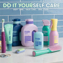 Frida for Kids body wash, shampoo, deodorant, and oral care products arranged on a white countertop against a blue tiled background.