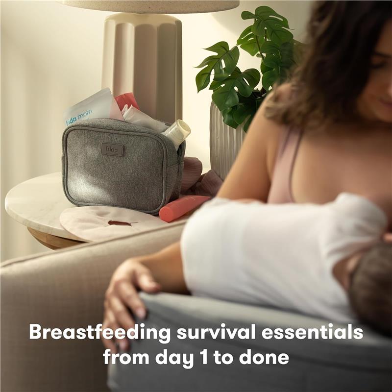Frida Mom 13Pk Breastfeeding Survival Kit in a gray bag on a table beside a nursing mother and baby, featuring various breastfeeding essentials.