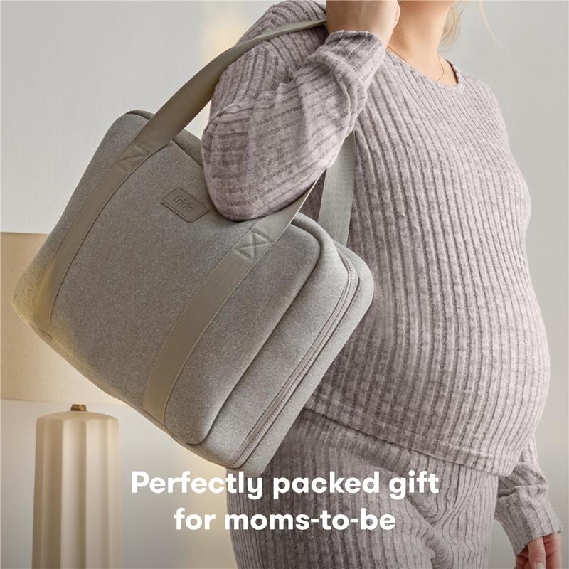 Frida Mom 30Pk hospital and baby essential travel bag, held by a pregnant woman in a cozy outfit, with text below.