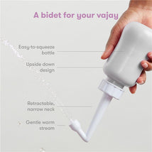 Gray Frida Mom Upside Down Peri Bottle sprayer held by a hand, demonstrating a gentle warm stream of water for postpartum care.