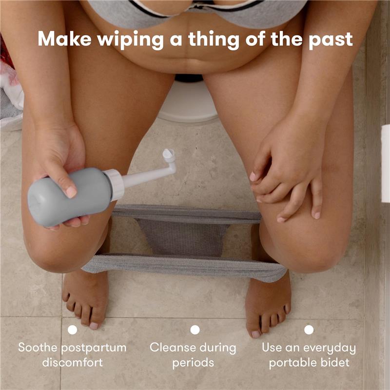 Gray Frida Mom Upside Down Peri Bottle being held by a person seated on a toilet, with text highlighting postpartum care benefits.