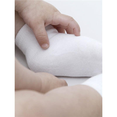 White baby socks from the Gerber Baby 6-Pair Sock Bundle, with a hand reaching for one sock.
