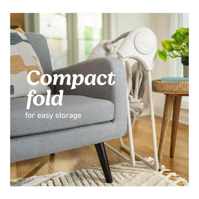 Graco Slim Spaces 2.0 Swing in compact fold position beside a grey couch, emphasizing easy storage feature.