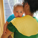 Organic muslin burp cloth draped over the shoulder of a caregiver holding a baby, both looking out a window.