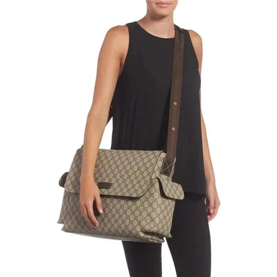 Gucci Supreme Beige diaper bag being held by a woman in a black sleeveless top, featuring the iconic logo pattern.