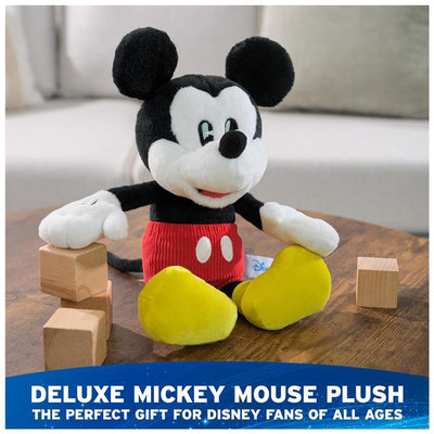 Deluxe plush Mickey Mouse toy with red shorts and yellow shoes, sitting near wooden blocks on a table.