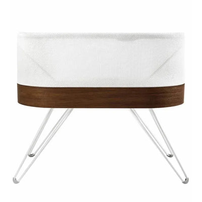 SNOO Smart Sleeper Bassinet with a white mesh fabric and walnut wood base on sleek metal legs.