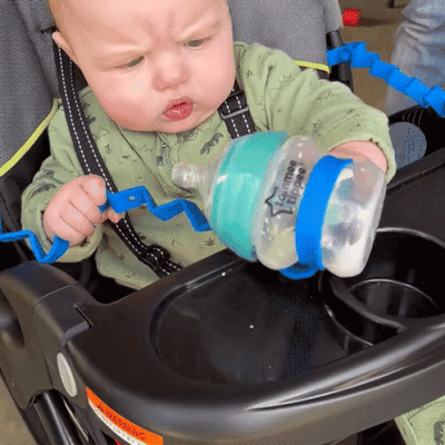 Baby using a Busy Baby Mat bottle bungee to secure a feeding bottle in a stroller.