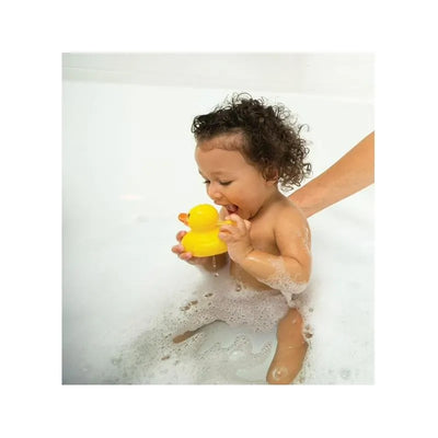 Baby with curly hair playing in a bubble bath, holding a yellow rubber duck, with a hand gently supporting them.