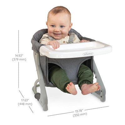 Baby seated in the Infantino Ultimate Travel Booster with a gray fabric seat, white tray, and visible dimensions beside.