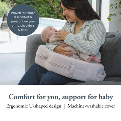 A woman smiles while holding a baby on an Inglesina Elysia Nursing Pillow in delicate pink, showcasing its U-shaped design.