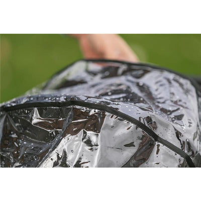 Inglesina Quid³ stroller raincover with water droplets on a transparent surface, being held by a hand outdoors.