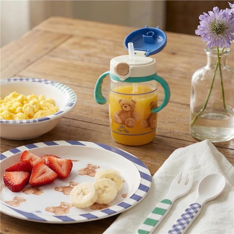 Itzy Ritzy Itzy Sips straw cup with snap-close lid, filled with juice, beside a plate of sliced strawberries and bananas.