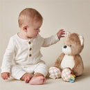Infant interacting with a soft Itzy Ritzy Snuggles Plush Bear toy, featuring a light brown color and checkered details.