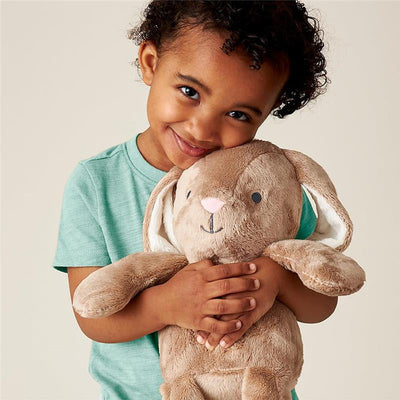 A child hugs a taupe plush bunny toy with floppy ears and a cute face, smiling happily.