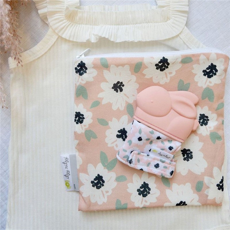 Teething mitt featuring a pink bunny design, placed on a floral-patterned pouch and a textured fabric backdrop.