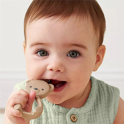 Baby holding a Toast Bear 360-degree training toothbrush, smiling with the brush in their mouth.