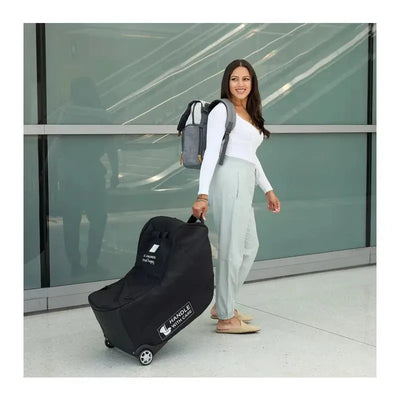 Black J.L. Childress car seat travel bag with wheels, carried by a woman in an airport terminal.