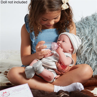 A girl holds a baby doll with a pink bottle, gently feeding it while seated on a soft blanket.