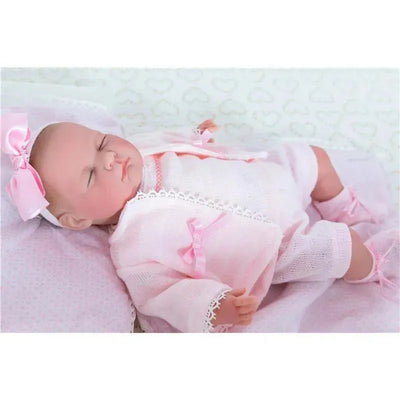 Realistic baby doll wearing a pink outfit with bows and lace, lying on a soft blanket with a serene expression.
