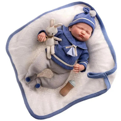 Reborn doll Mateo dressed in a sailor blue outfit, holding a bunny toy, resting on a white blanket.