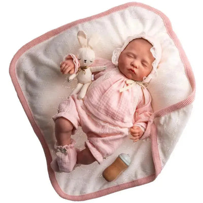 Reborn doll, Sofia, dressed in pink, lying on a blanket with a bunny toy and a bottle nearby.