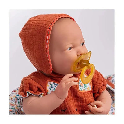 JC Toys La Newborn baby doll with a soft body, wearing a nature-themed outfit and holding a yellow pacifier.